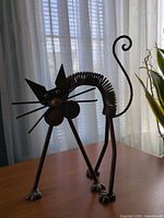Front view of iron cat sculpture showing coiled body, facial features, and stance