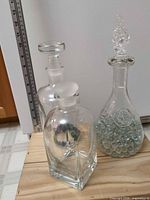 Three clear glass decanters with stoppers and marbles displayed together