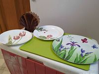 Three floral Corelle plates and wooden puzzle box displayed on counter