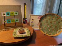 Group shot of fused glass panel on stand, paperweight on dish, square floral plate and round plate