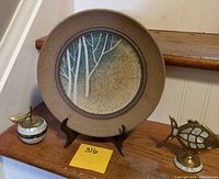Front view of stoneware plate on stand with brass apple box and brass fish figurine