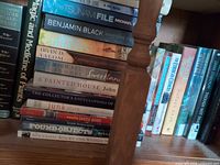 Books stacked on shelf showing multiple spines including The Tsunami File, Christine Falls, Summer at Tiffany’s, Sweetland, A Painted House, Magic and Medicine of Plants, North American Wildlife, The Collector’s Encyclopedia of Shells, Junk Style, Found Objects, New Craft: Sticks and Stones
