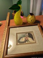 Lot overview showing tall glass bird, small glass bird, framed puffin print, ruler for scale