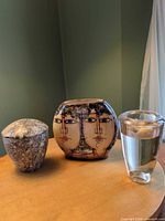 Three decorative vessels side by side: marble jar with lid, Arroyabe two-face vase, glass candleholder