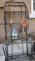 Full view of black metal baker's rack with glass shelf and hanging decor items