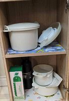Rice cooker parts, small bowls and lids on shelf alongside boxed water bottle