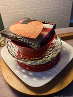 Stacked lot showing boxed bread warmer, red nested bowls inside clear hobnail bowl, on Corelle plate and wood board