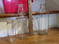 Group of four clear glass milk bottles next to ruler for scale