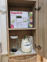 Both items stored in cabinet: Starfrit spiralizer boxed on shelf, Oster blender base and jar below