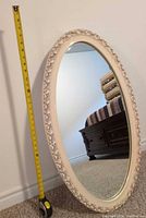 Front view showing oval mirror, ornate ivory frame, tape measure indicating size