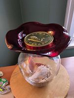 Vase with ruffled ruby rim, clear body filled with seashells, coin bank resting on top