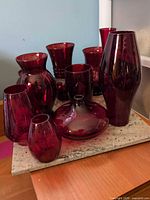 Front view of all ten ruby red glass vases on stone slab