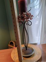 Tall metal candle holder with red candle, bead garland, ruler for height reference, ceramic plate visible
