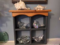 Overall view of glass bird figurines on and in display shelf with seashells on top