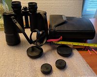 Binoculars standing beside closed carrying case, strap visible, lens caps laid out, tape measure nearby