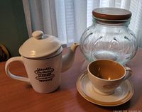 Teapot, teacup, saucer and glass jar with wood lid grouped on tabletop