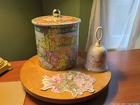 Tin canister with lid beside porcelain bell on wooden surface
