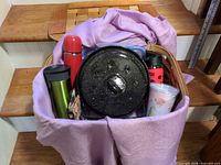 Basket filled with blanket, cookware lid, thermoses and travel mugs