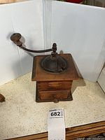 Front view showing wooden body, cast iron lid, crank handle, drawer