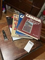 Stack of four Canada hardcover books and small black resin totem pole on table