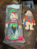 Both plush figures side by side, Lucky Leprechaun sealed in bag, Fred Flintstone worn
