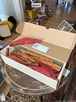 Open cardboard box showing assorted Lincoln Logs pieces in natural, red and green wood