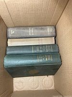 Four books in box showing spines: gray, cream, two green
