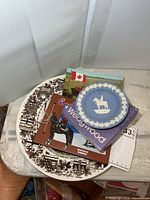 Stack showing large RCMP plate, Wedgwood dish, postcard, booklet and album