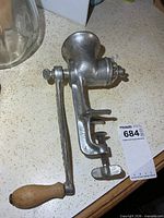 Full view of cast metal meat grinder with wooden handle and clamp screw visible