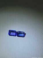 Pair of emerald-cut violet-blue tanzanites on neutral background