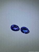 Pair of oval deep blue tanzanite gemstones on light background