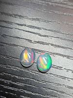 Two oval cabochon opals on dark surface showing play of color