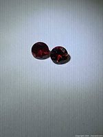 Pair of round brilliant cut red garnets on neutral background