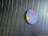 Front view of oval cabochon opal on textured surface showing multicolour play-of-colour