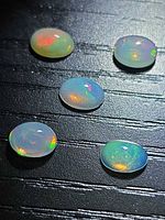 Five oval opal cabochons on dark background showing play of colour