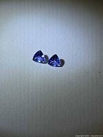 Pair of violet-blue trillion tanzanites on neutral background
