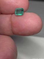 Octagon-cut green emerald resting on fingertip