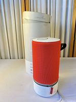 Speaker with red/orange sleeve beside original white cylindrical box