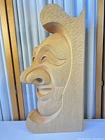 Front angled view of entire wood relief mask showing stylized face and textured background