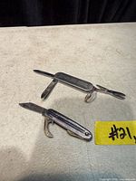 Both pocket knives open showing blades and tools