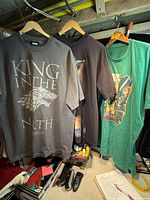 Three T-shirts on hangers: Game of Thrones, cowgirl graphic, illustrated green shirt