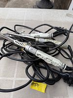 Three light grey handled curling irons with cords