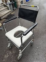 Front left view of commode chair showing chrome frame, white seat, armrests, casters