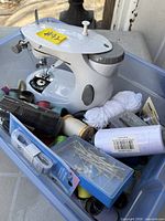 Bin containing mini sewing machine and assortment of sewing supplies