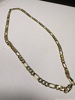 Full view of gold-tone Figaro chain necklace with lobster clasp