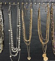 Group view of silver-tone faux pearl necklace, gold-tone heart charm necklace, gold-tone coin pendant necklace, and part of purple stone necklace