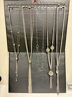 Full view of six silver-tone lariat/tassel necklaces on display board