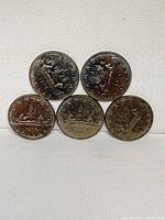 Fronts of five 1975 Voyageur dollars arranged in two rows