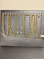 Seven gold-tone chain necklaces displayed side by side on black background