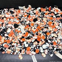 Wide view of entire assortment of orange, white and black cameo cabochons spread on surface